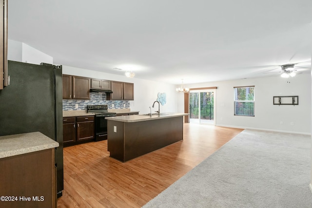 kitchen featuring a kitchen island with sink, black fridge, electric stove, light wood-type flooring, and dark brown cabinetry