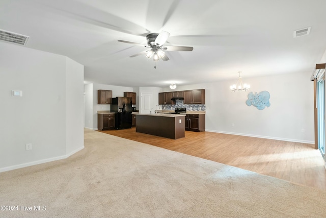 kitchen featuring decorative backsplash, black appliances, light hardwood / wood-style floors, hanging light fixtures, and an island with sink