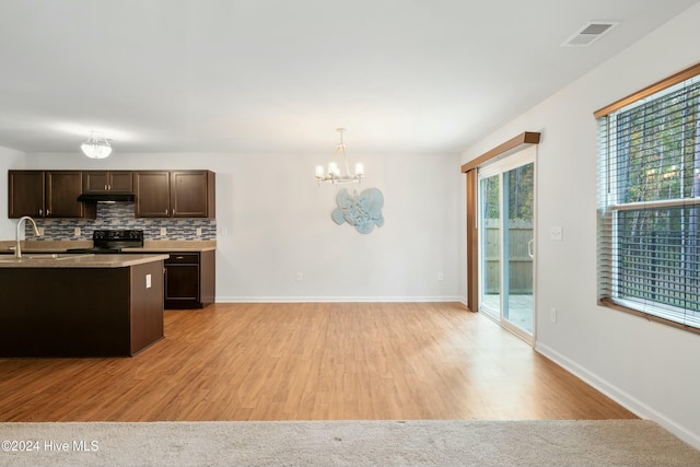 kitchen featuring backsplash, black stove, decorative light fixtures, and light wood-type flooring