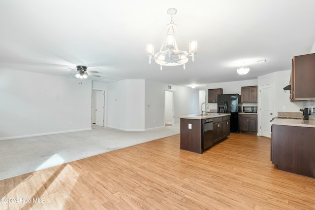 kitchen with ceiling fan with notable chandelier, black appliances, decorative light fixtures, light hardwood / wood-style flooring, and an island with sink