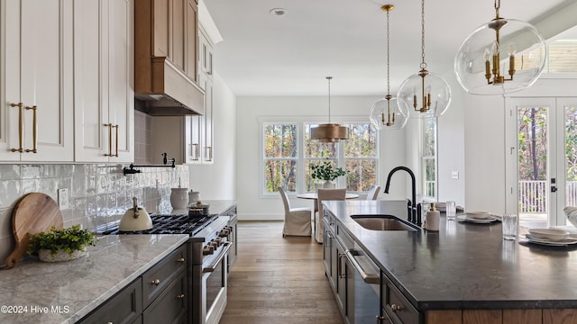 kitchen with dark wood-type flooring, sink, dark stone countertops, an island with sink, and appliances with stainless steel finishes