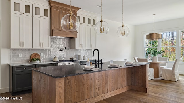 kitchen with a kitchen island with sink, dark wood-type flooring, sink, decorative light fixtures, and white cabinetry