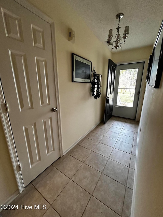 doorway with light tile patterned floors, a textured ceiling, and an inviting chandelier