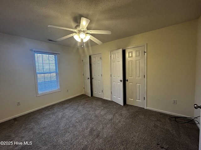 unfurnished bedroom with dark colored carpet, a textured ceiling, ceiling fan, and multiple closets