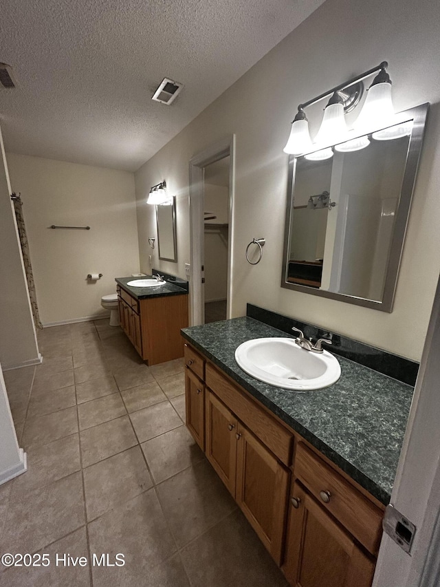 bathroom with tile patterned flooring, a textured ceiling, vanity, and toilet