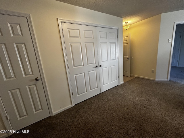 unfurnished bedroom featuring a textured ceiling, dark carpet, and a closet