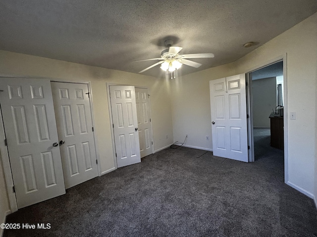 unfurnished bedroom with a textured ceiling, two closets, dark carpet, and ceiling fan