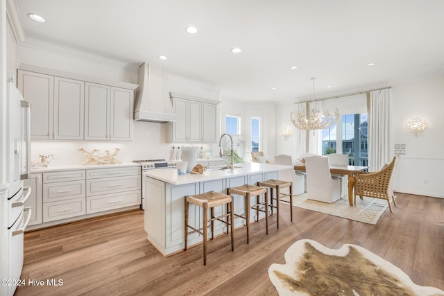 kitchen featuring premium range hood, high end white refrigerator, a center island with sink, a notable chandelier, and light hardwood / wood-style floors