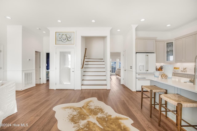 kitchen featuring a breakfast bar area, a kitchen island with sink, white cabinets, custom range hood, and light wood-type flooring