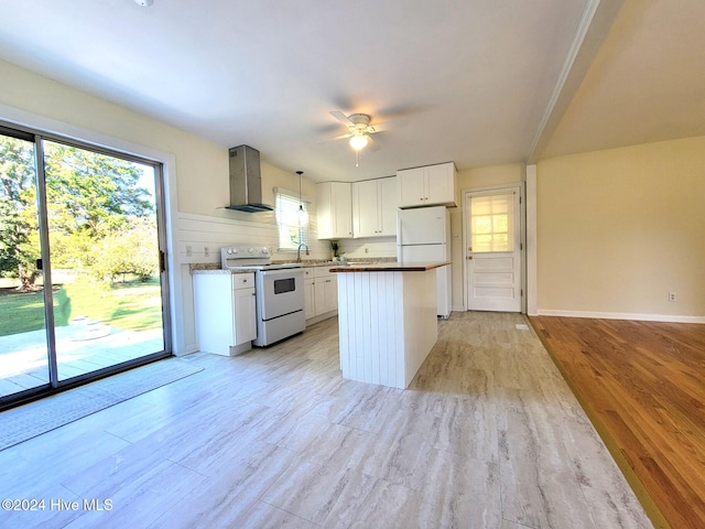 kitchen with wall chimney range hood, white cabinetry, hanging light fixtures, and white appliances