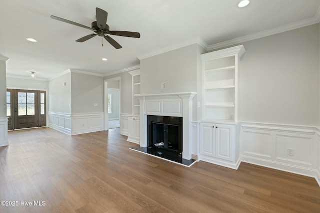 unfurnished living room with built in features, recessed lighting, a ceiling fan, a decorative wall, and wood finished floors