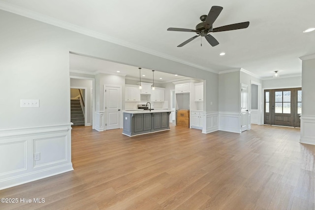 unfurnished living room featuring ornamental molding, ceiling fan, light wood finished floors, recessed lighting, and stairs
