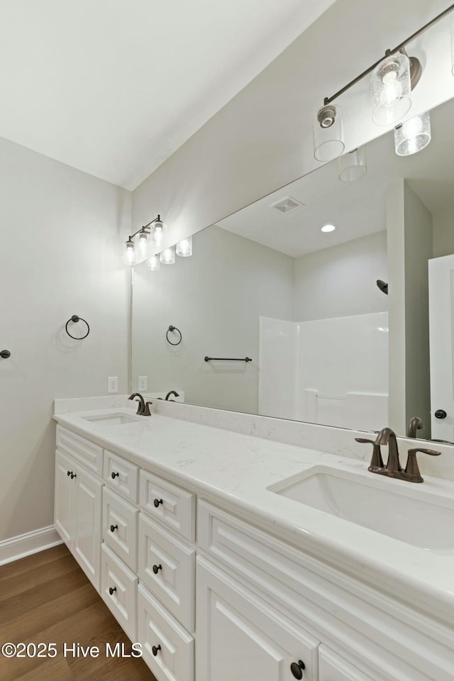 bathroom featuring wood finished floors, double vanity, a sink, and visible vents
