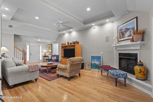 living room featuring a raised ceiling, ceiling fan, light hardwood / wood-style floors, and ornamental molding