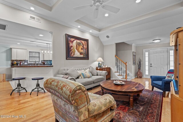 living room with sink, crown molding, ceiling fan, light wood-type flooring, and a tray ceiling