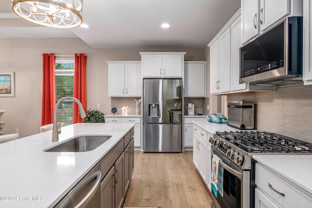 kitchen featuring white cabinets, sink, light wood-type flooring, decorative light fixtures, and stainless steel appliances