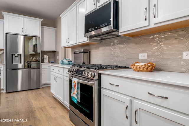 kitchen with appliances with stainless steel finishes, light wood-type flooring, tasteful backsplash, and white cabinetry