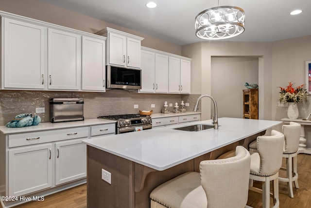 kitchen featuring a kitchen island with sink, sink, light hardwood / wood-style flooring, appliances with stainless steel finishes, and white cabinetry