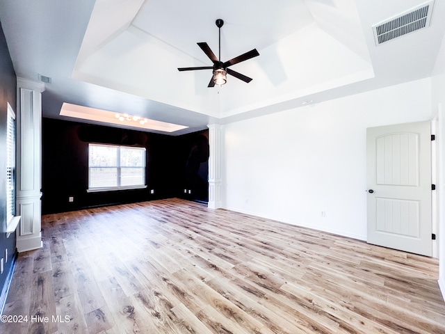 unfurnished living room featuring a raised ceiling, ceiling fan, and light hardwood / wood-style flooring