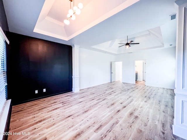 unfurnished living room featuring ceiling fan with notable chandelier, a raised ceiling, and light wood-type flooring