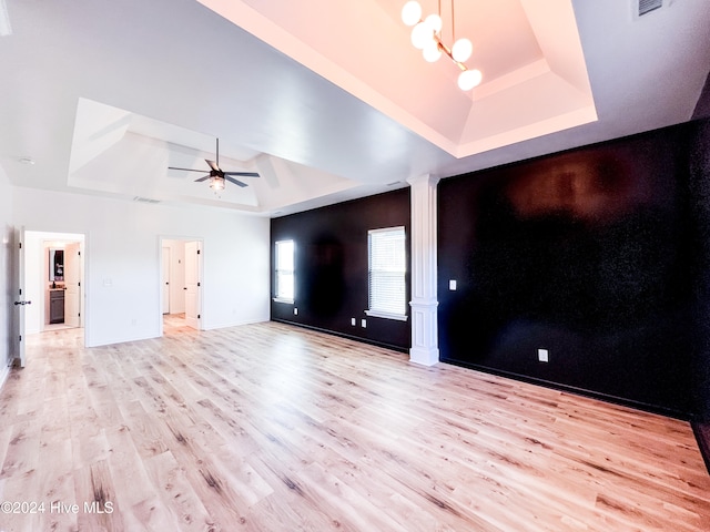 unfurnished living room featuring ceiling fan with notable chandelier, a tray ceiling, and light hardwood / wood-style flooring