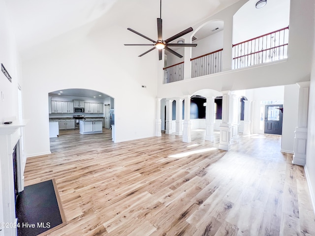 unfurnished living room with a high ceiling, light wood-type flooring, ornate columns, and ceiling fan