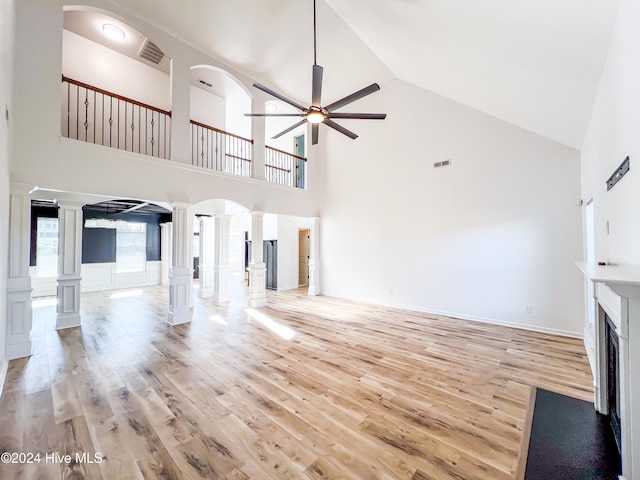 unfurnished living room with decorative columns, ceiling fan, high vaulted ceiling, and light wood-type flooring