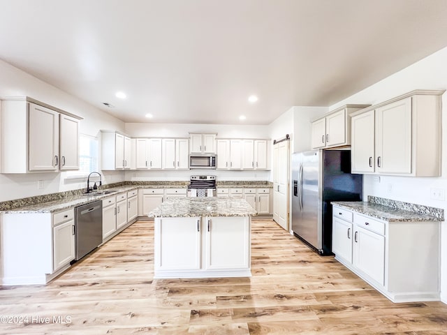 kitchen with a center island, white cabinets, sink, appliances with stainless steel finishes, and light stone counters