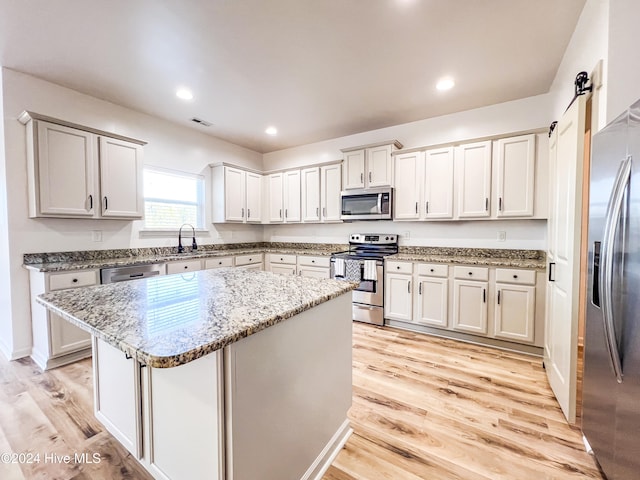 kitchen with a center island, a barn door, light stone countertops, light hardwood / wood-style floors, and stainless steel appliances