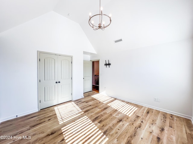 unfurnished bedroom with a closet, high vaulted ceiling, light hardwood / wood-style flooring, and an inviting chandelier