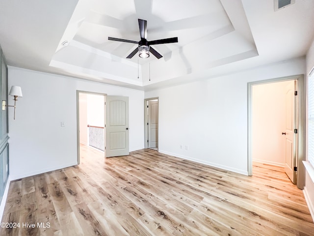 unfurnished bedroom featuring a tray ceiling, ceiling fan, and light hardwood / wood-style floors