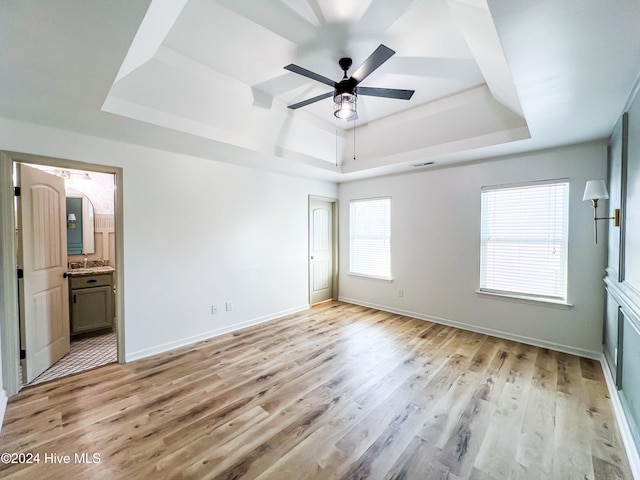 unfurnished bedroom featuring light wood-type flooring, connected bathroom, a tray ceiling, and ceiling fan