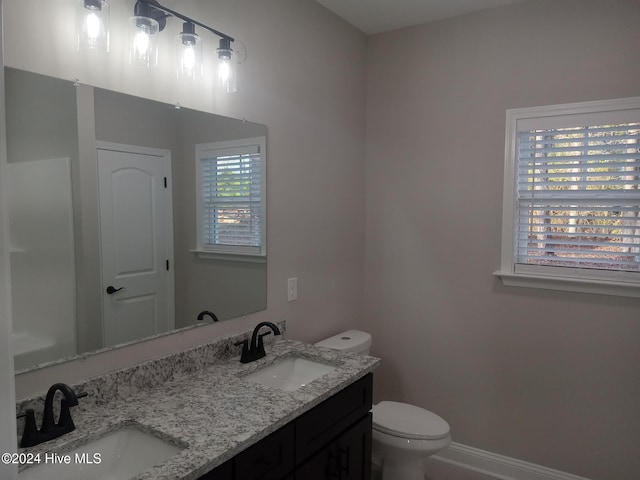 bathroom with a sink, baseboards, toilet, and double vanity