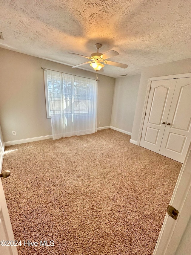 empty room with carpet flooring, ceiling fan, and a textured ceiling