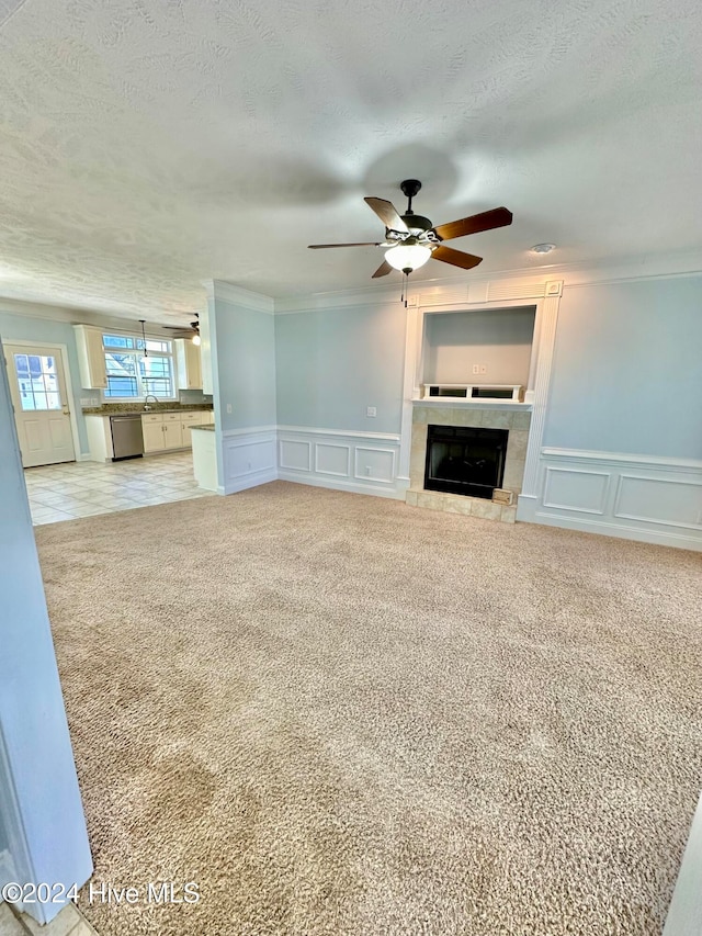 unfurnished living room featuring ceiling fan, ornamental molding, a textured ceiling, light colored carpet, and a tiled fireplace