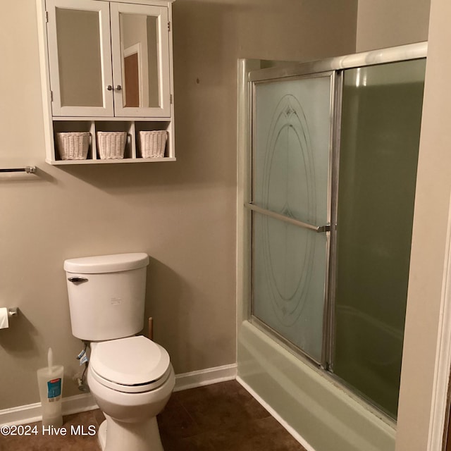 bathroom with tile patterned flooring, toilet, and bath / shower combo with glass door