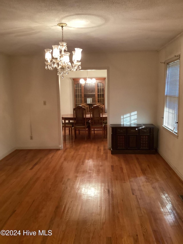 unfurnished dining area featuring hardwood / wood-style flooring, a textured ceiling, and an inviting chandelier