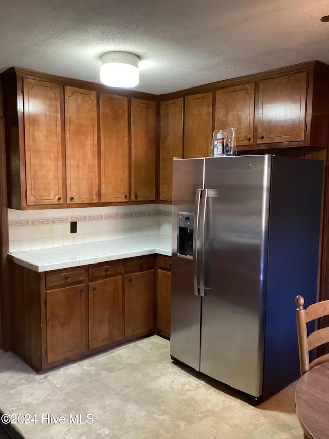 kitchen with stainless steel fridge with ice dispenser, a textured ceiling, tasteful backsplash, and tile counters