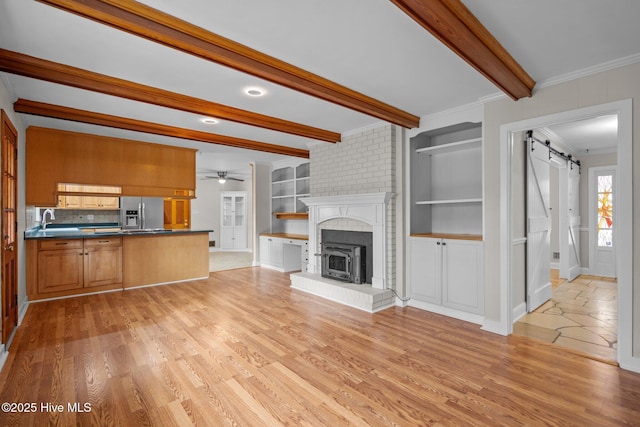 unfurnished living room featuring light wood-type flooring, ornamental molding, sink, a barn door, and built in features