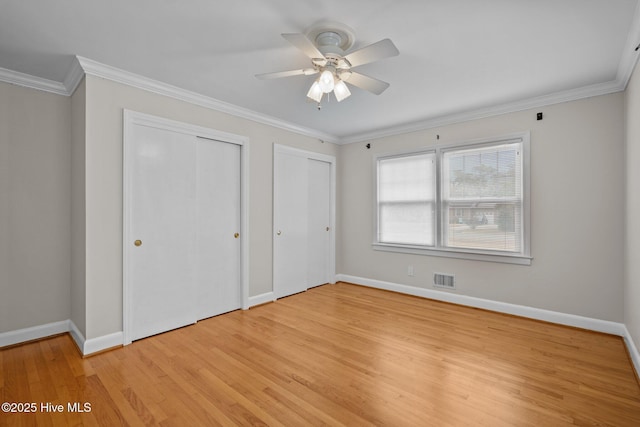 unfurnished bedroom with ceiling fan, light wood-type flooring, crown molding, and two closets