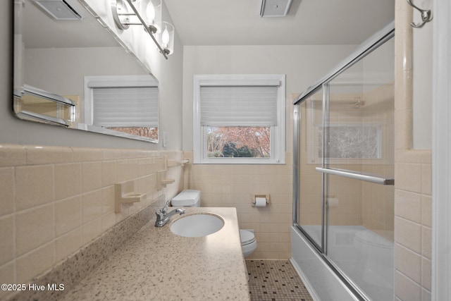 full bathroom featuring vanity, shower / bath combination with glass door, tile patterned floors, toilet, and tile walls