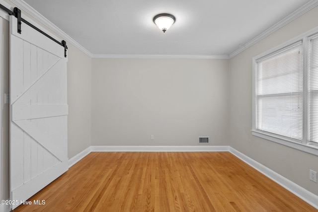 unfurnished room with a barn door, wood-type flooring, and ornamental molding