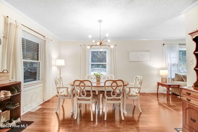 dining area with a textured ceiling, a notable chandelier, light wood-type flooring, and crown molding