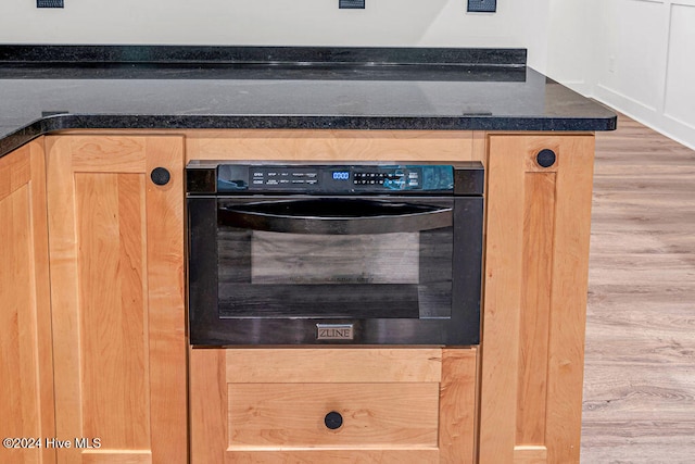 details with light brown cabinetry, oven, and hardwood / wood-style flooring