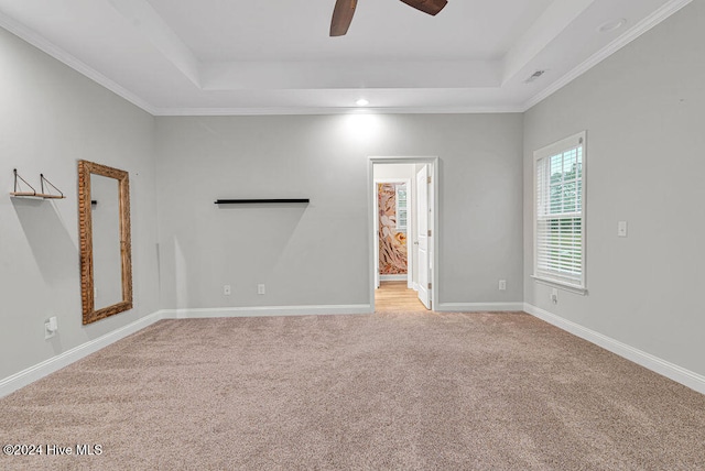 empty room with a tray ceiling, ceiling fan, light colored carpet, and ornamental molding