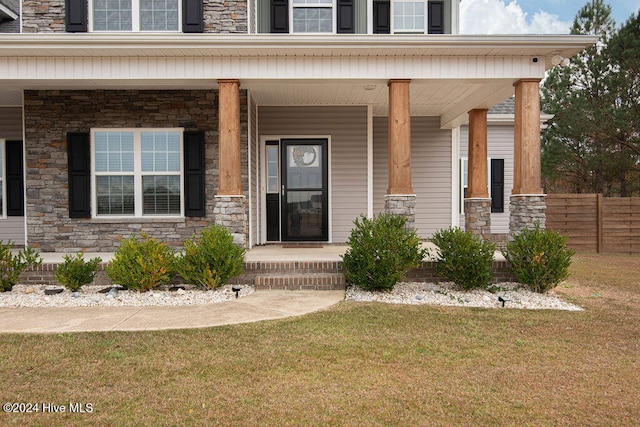 view of exterior entry with a lawn and covered porch