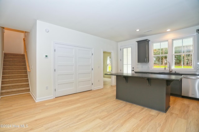 kitchen featuring stainless steel dishwasher, sink, light wood-type flooring, a center island, and a breakfast bar