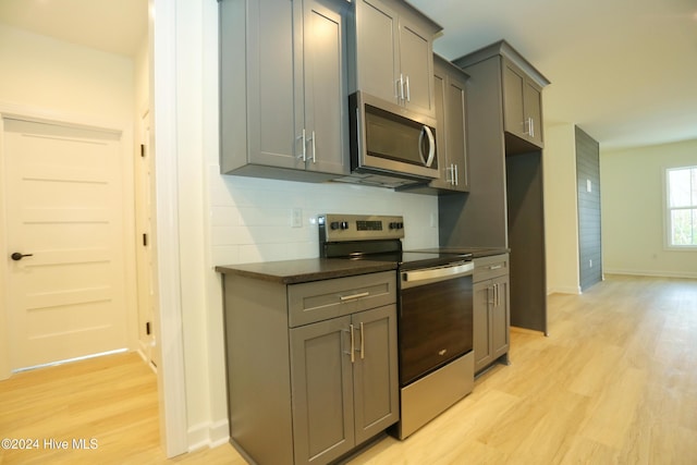 kitchen with light hardwood / wood-style flooring, appliances with stainless steel finishes, tasteful backsplash, and gray cabinets