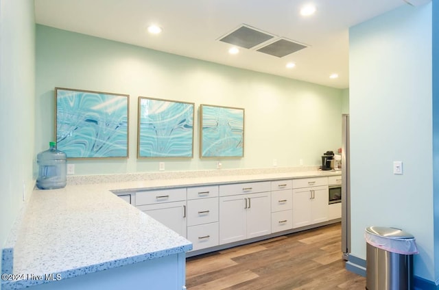 kitchen with white cabinetry, stainless steel microwave, light stone counters, and light wood-type flooring