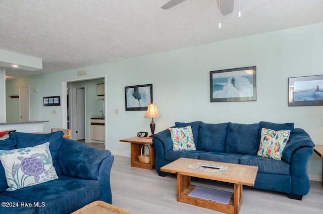 living room with ceiling fan, sink, light hardwood / wood-style floors, and a textured ceiling